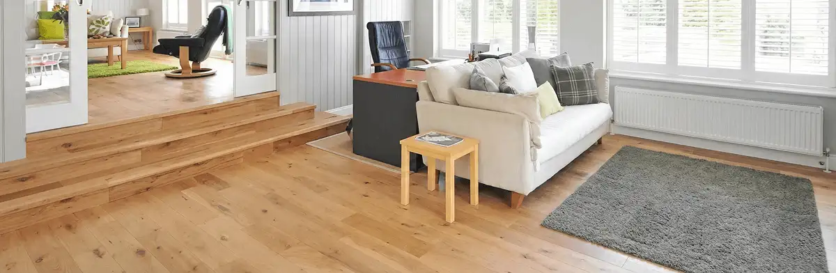 A modern living room with professionally installed laminate flooring, a beige sofa, a small side table, a gray rug, and large windows with white shutters in Savannah, GA
